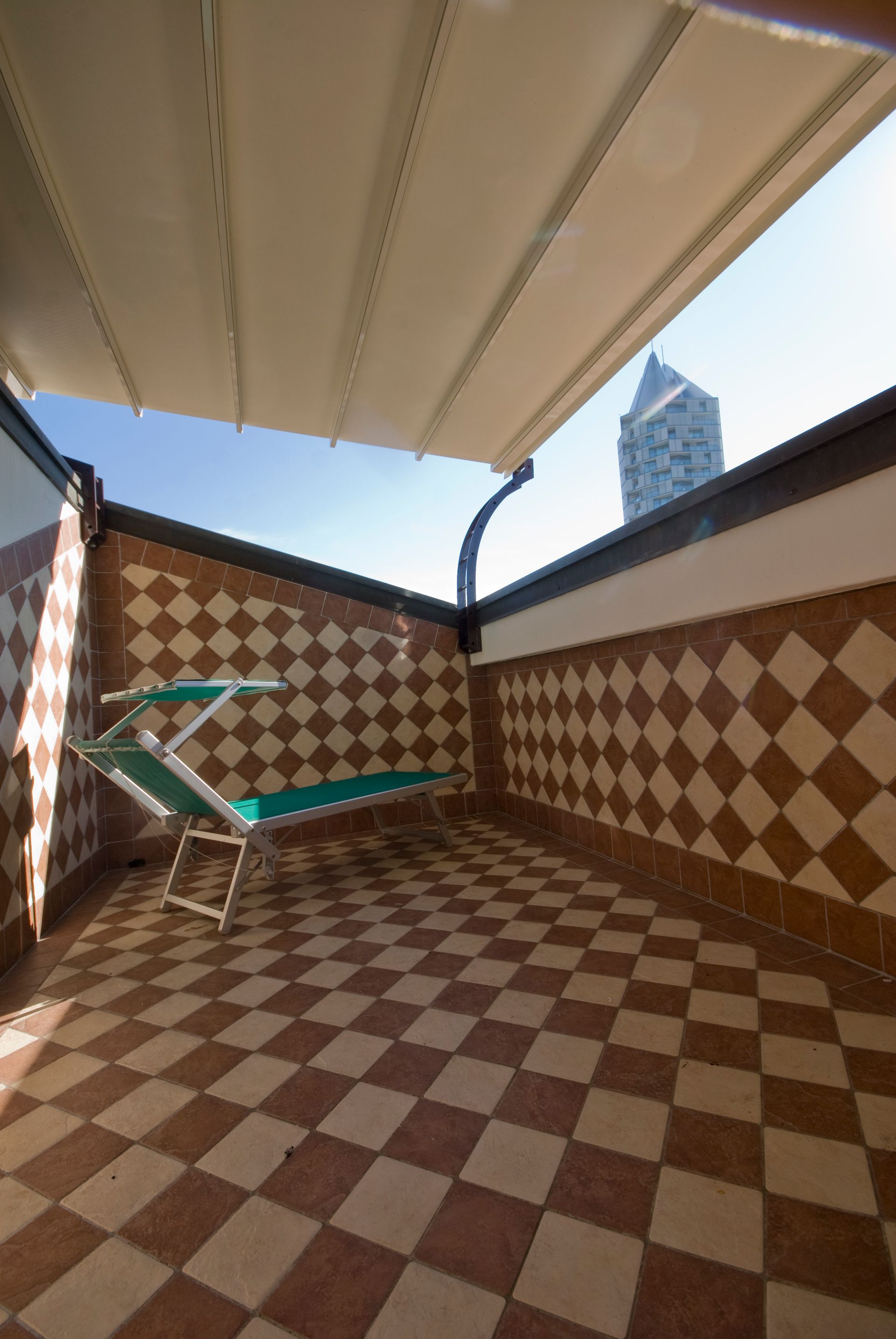 A balcony with a green chair and a checkered floor - Freehold, NJ - Awning Design Inc