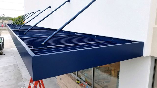 A blue awning is being installed on the side of a building - Freehold, NJ - Awning Design Inc
