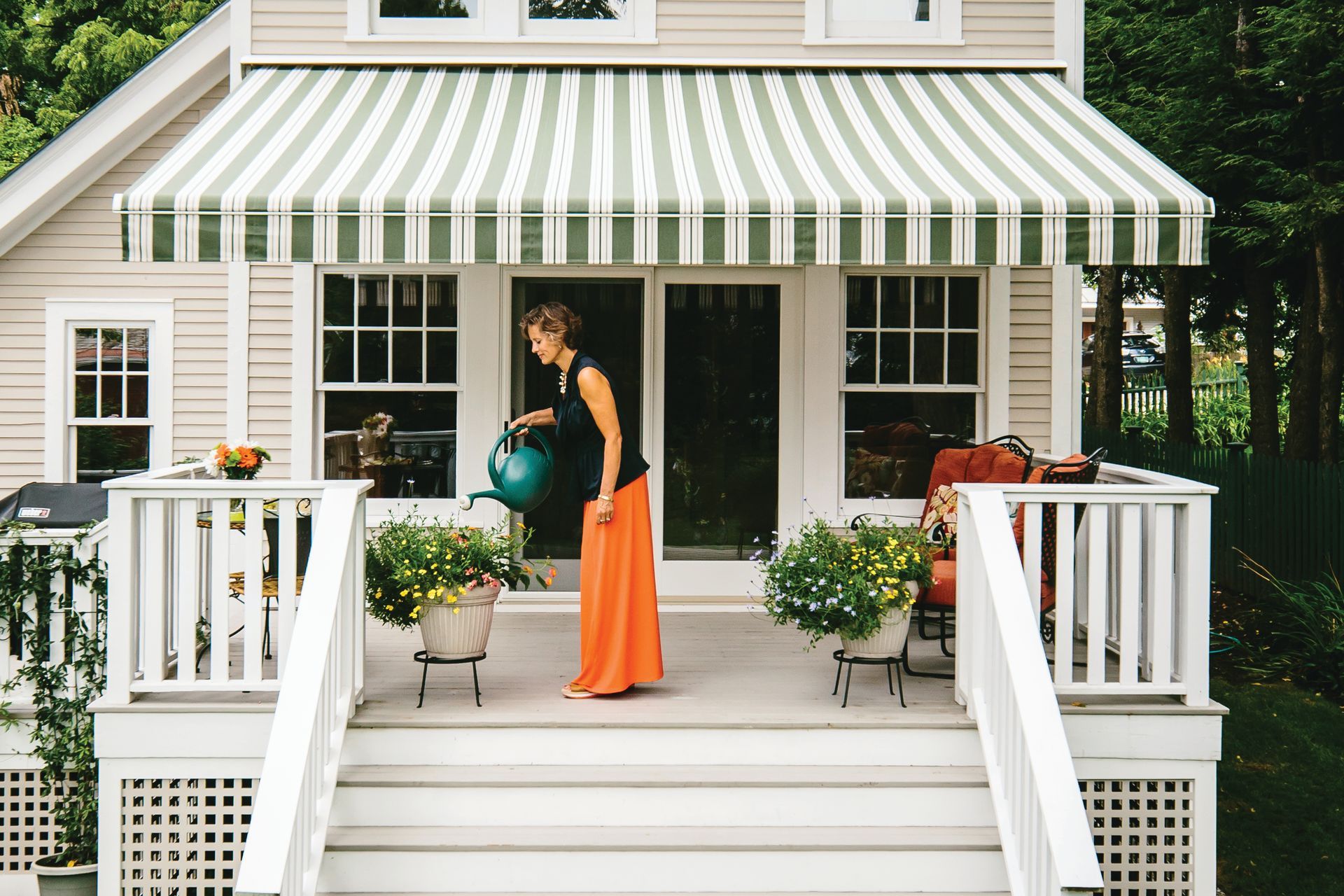 A woman is watering plants on the porch of a house - Freehold, NJ - Awning Design Inc