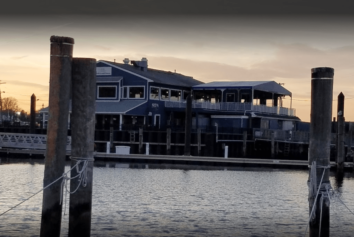 A large house is sitting on top of a body of water next to a dock - Freehold, NJ - Awning Design Inc