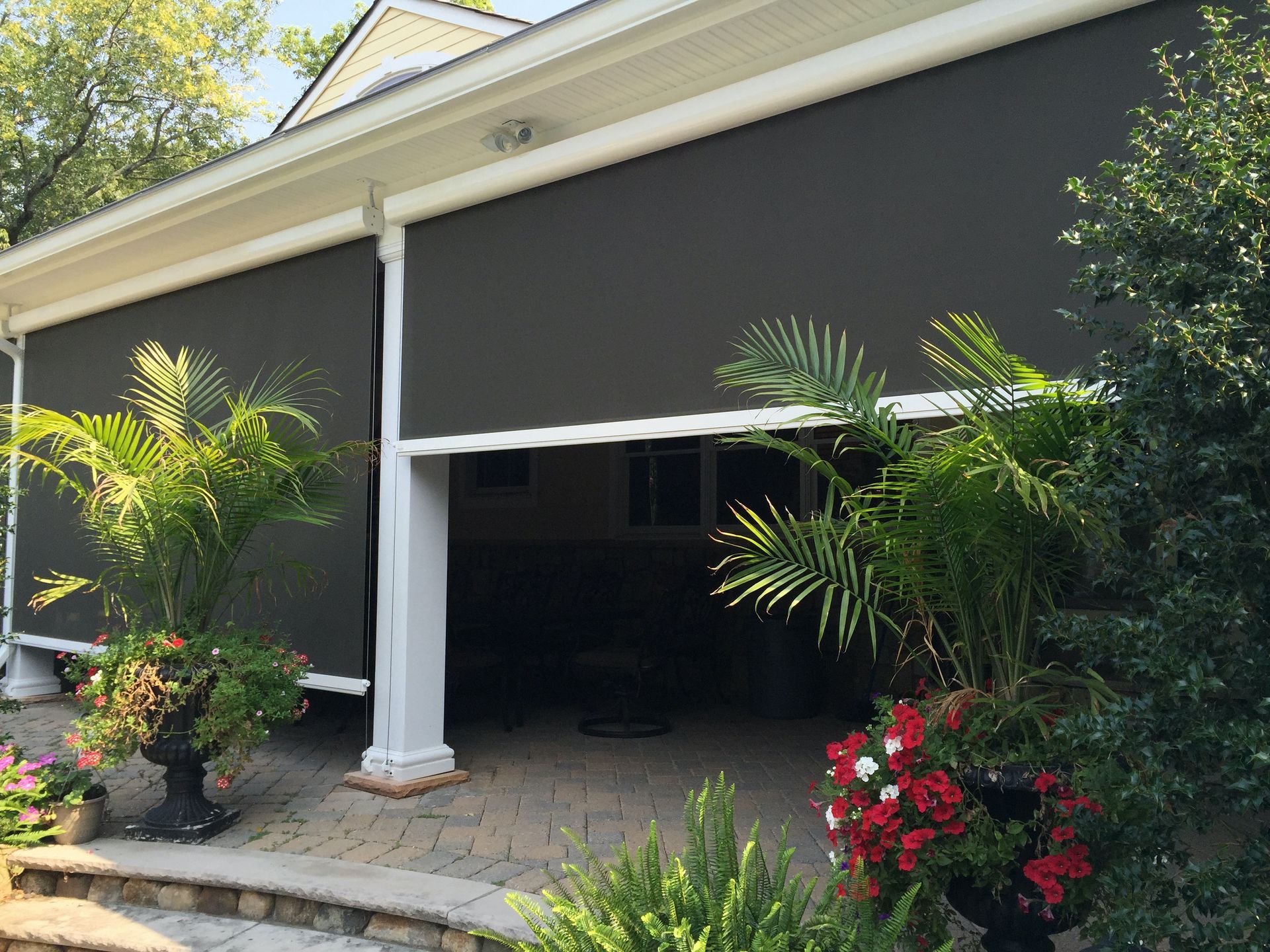 A house with a porch and a patio with a lot of plants and flowers - Freehold, NJ - Awning Design Inc