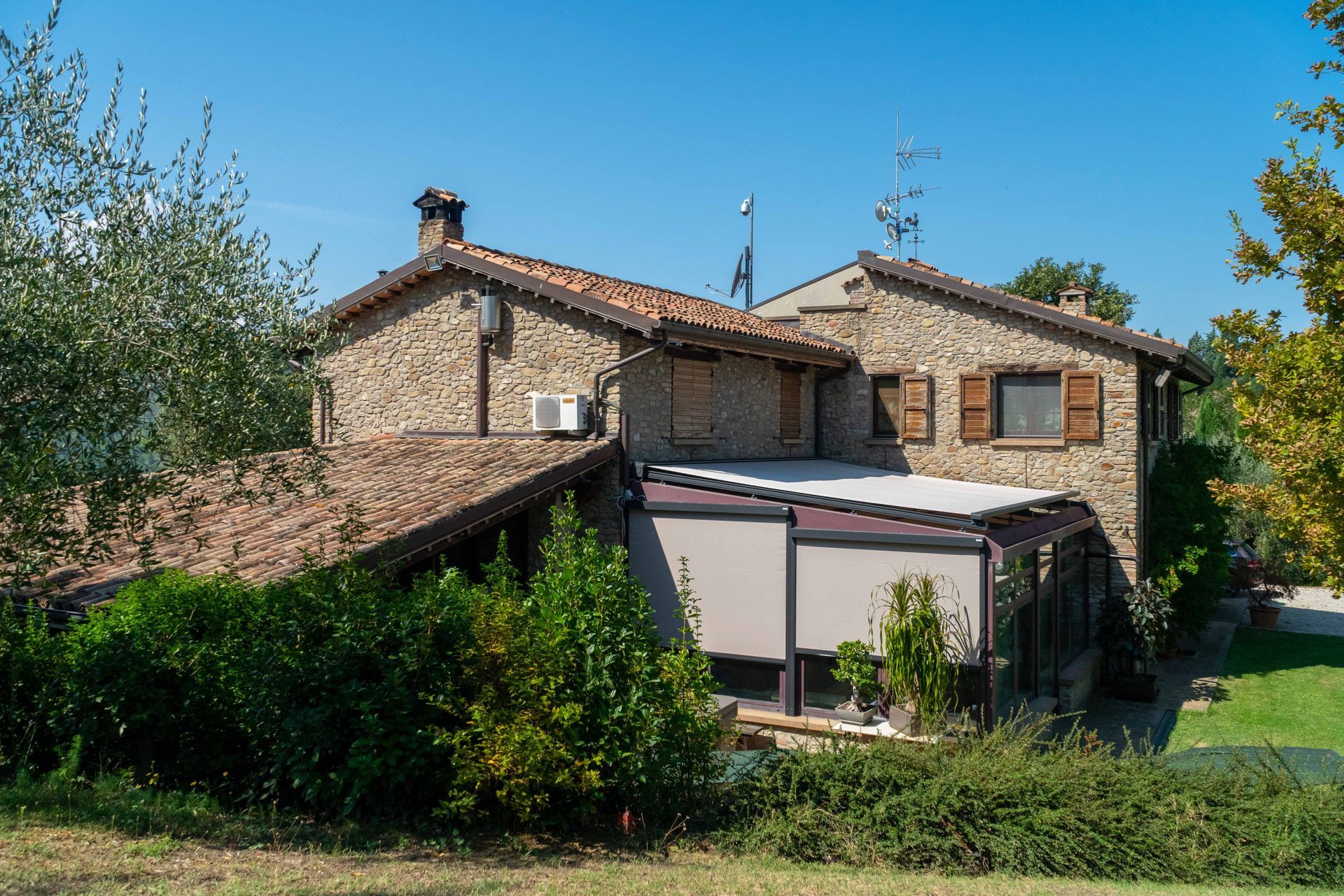 A large stone house is surrounded by trees and bushes on a sunny day - Freehold, NJ - Awning Design Inc