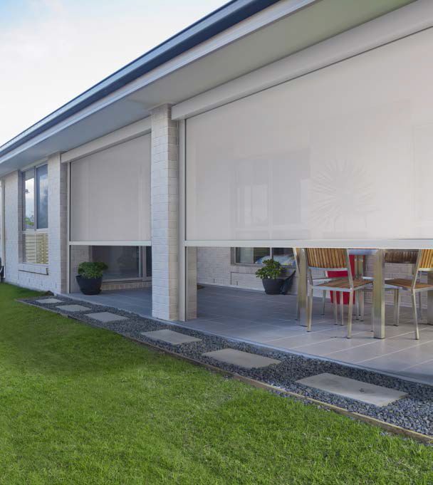 A house with a lot of windows and a patio with a table and chairs - Freehold, NJ - Awning Design Inc