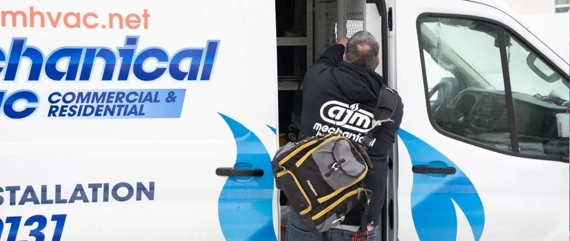 A technician with a tool bag enters a commercial van, the side of which displays a company logo for an HVAC business.