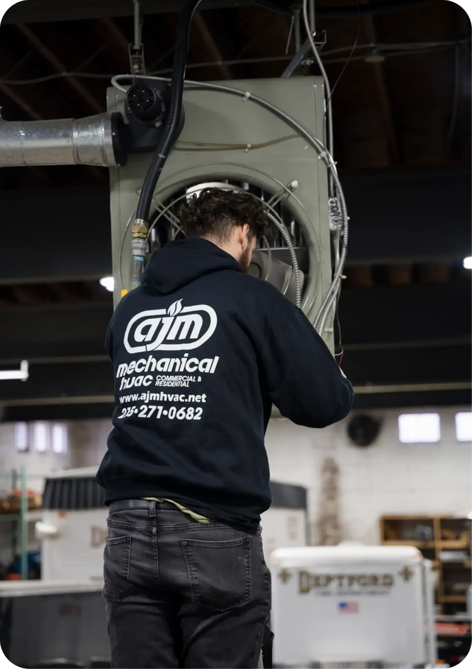 HVAC technician in a black hoodie works on overhead machinery in a commercial building.