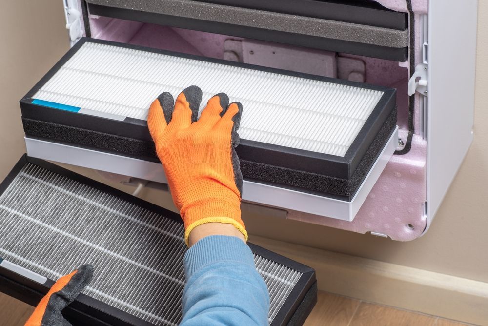 Person with orange gloves changing an air filter. The filters are white and black, and the unit is open.