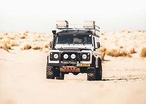 A white jeep is driving down a dirt road in the desert.