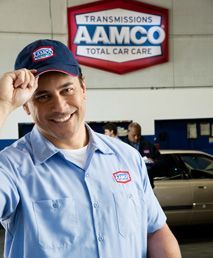 A man wearing a aamco hat stands in front of a car