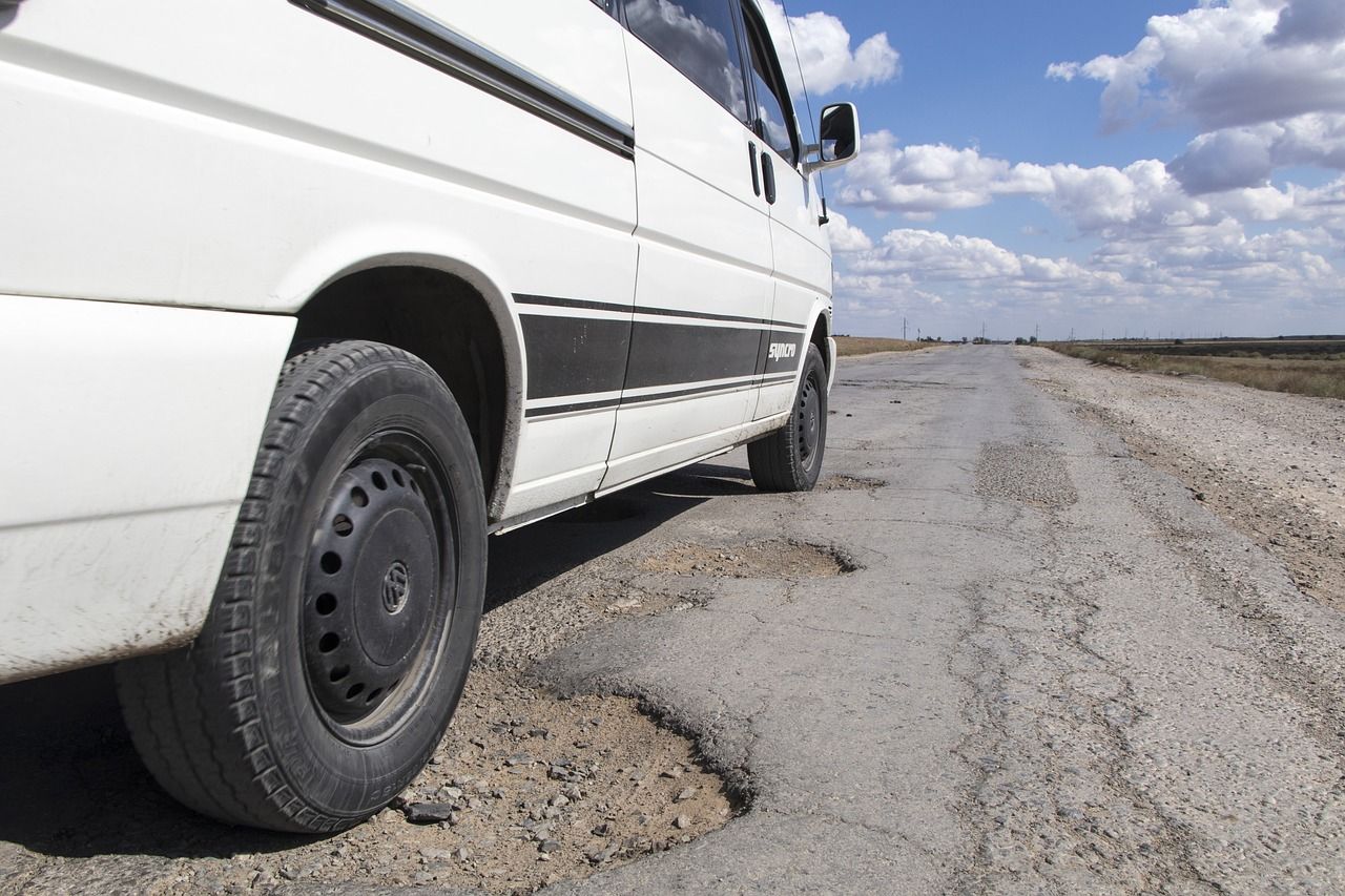 A white van is stuck in a pothole on a road.