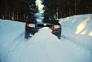 A car is driving through the snow on a snowy road