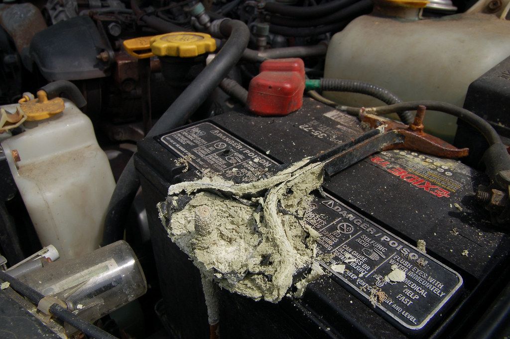 A close up of a car engine with a dirty battery