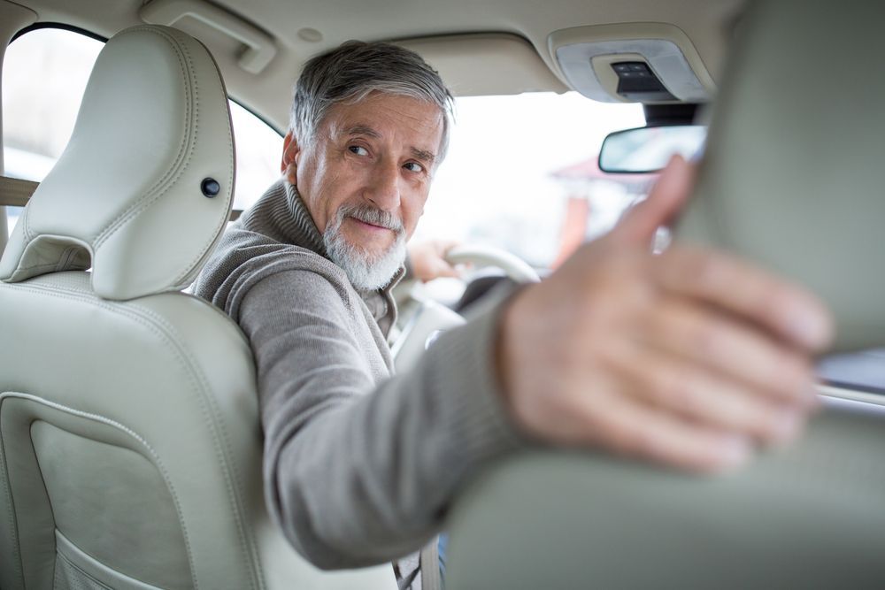 An older man is sitting in the back seat of a car giving a thumbs up.
