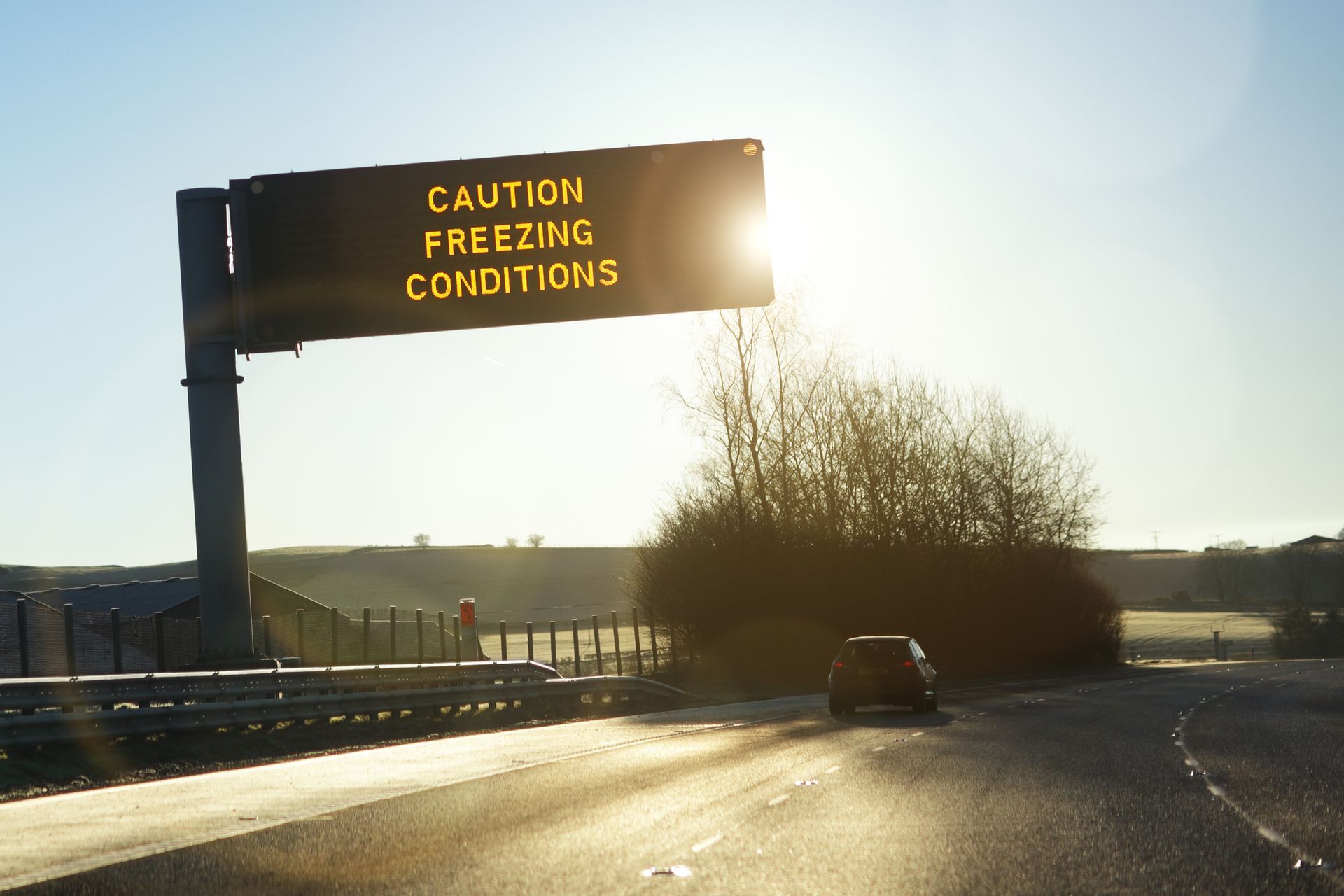 A car is driving down a highway under a sign that says caution freezing conditions