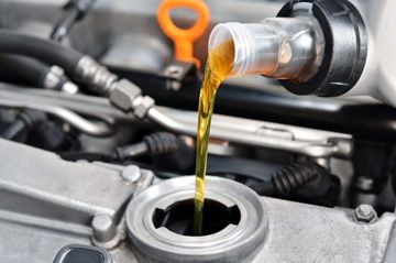 A close up of a person pouring oil into a car engine.
