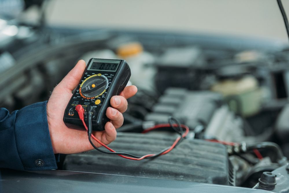 A person is holding a multimeter in front of a car engine.