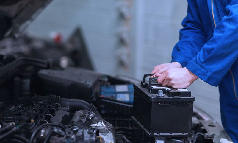A mechanic is fixing a car battery in a garage.