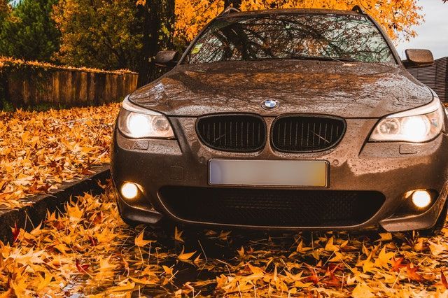 A bmw is parked in a pile of autumn leaves.
