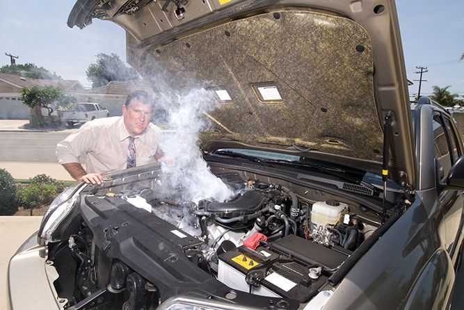 A man is looking under the hood of a car with the hood open