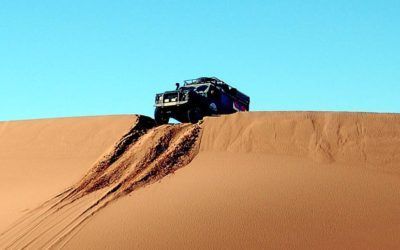 A jeep is driving down a sand dune in the desert