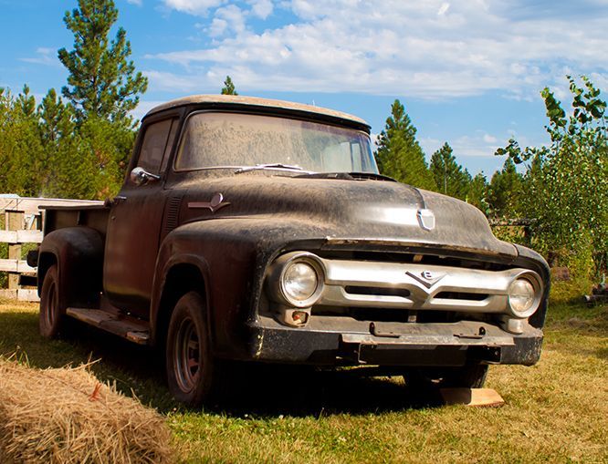An old dirty ford truck is parked in a grassy field