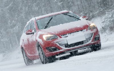 A red car is driving through the snow on a snowy road.