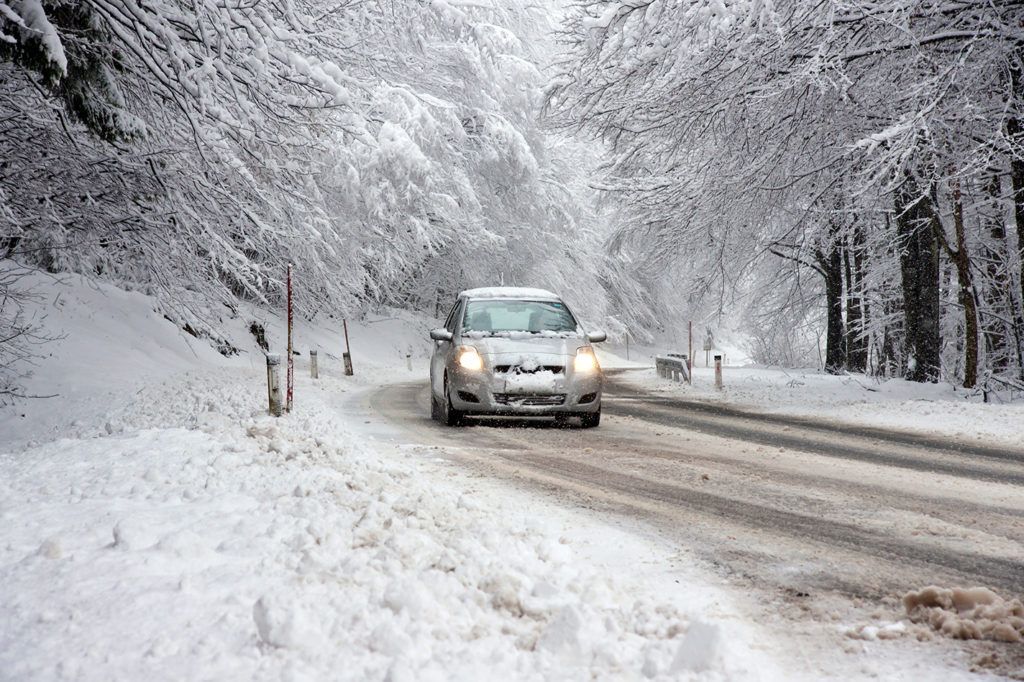 A car is driving down a snow covered road.