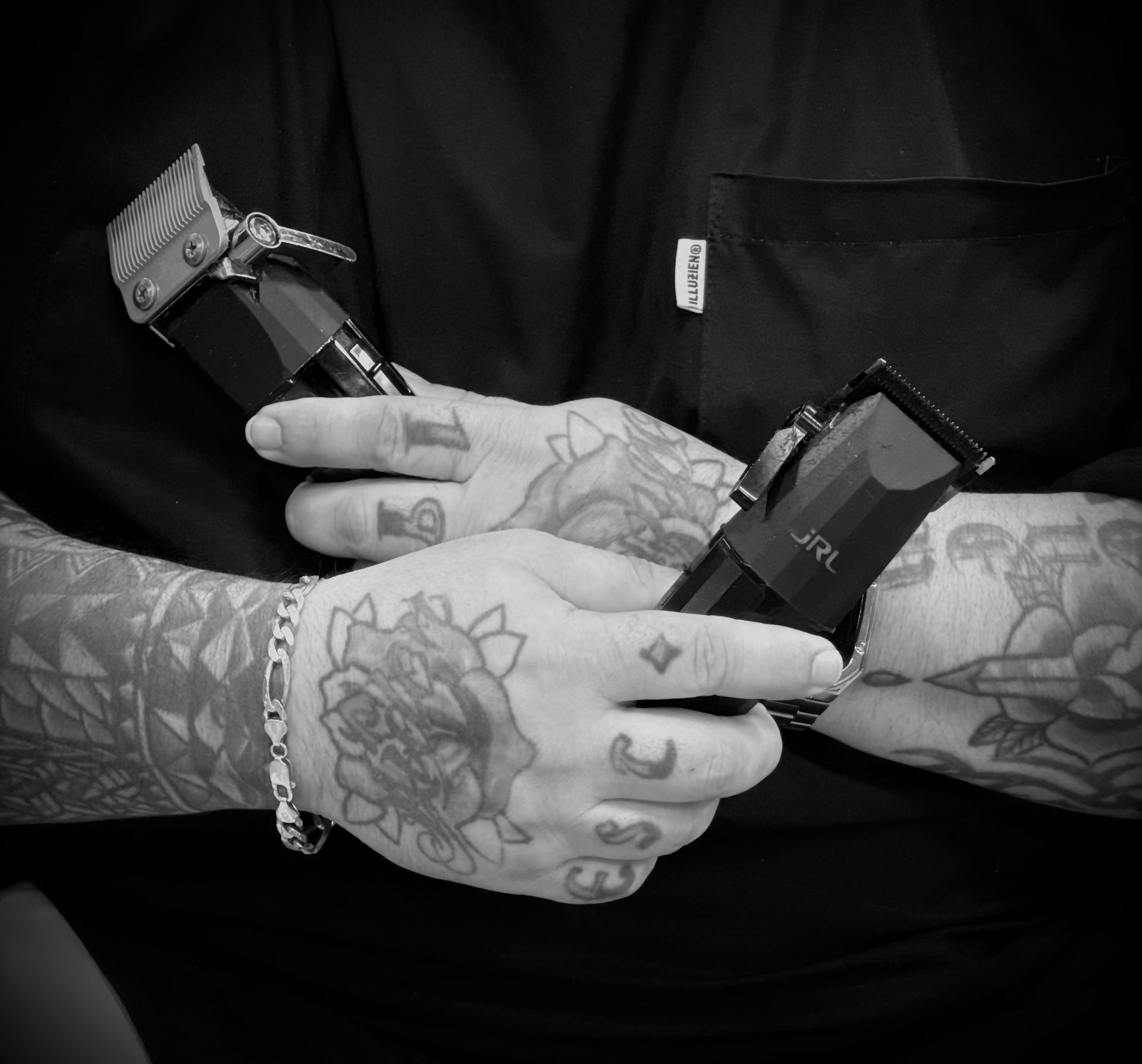 Tattooed hands holding two hair clippers, a black and white close-up.