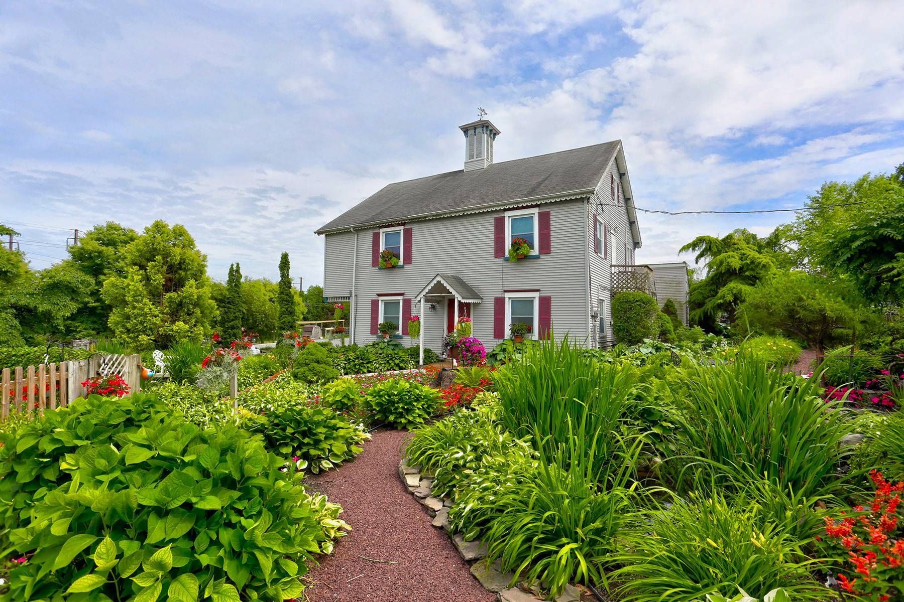 A large white house with pink shutters is surrounded by a lush green garden.