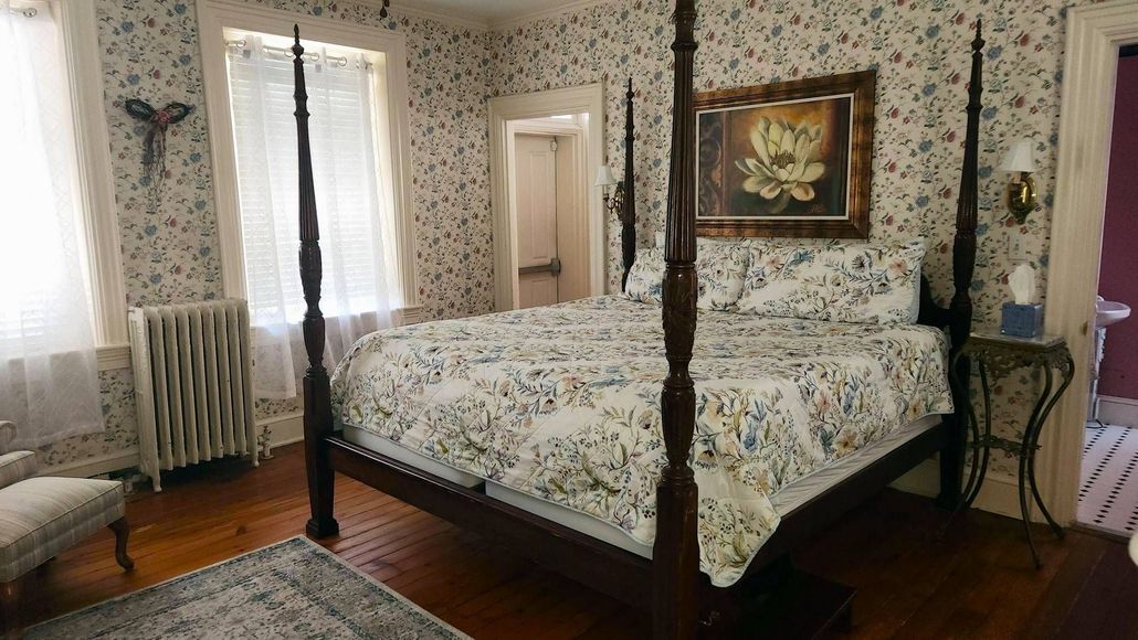 A bedroom with a four poster bed and a painting on the wall.
