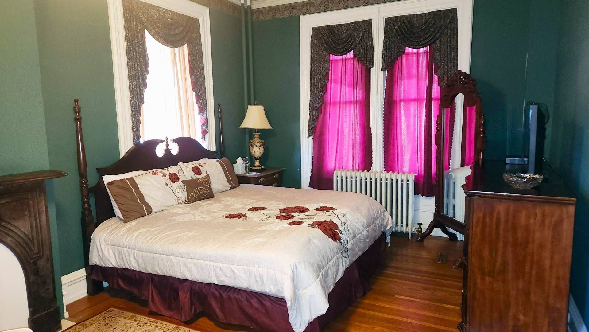 A bedroom with a bed , dresser , mirror and two windows.