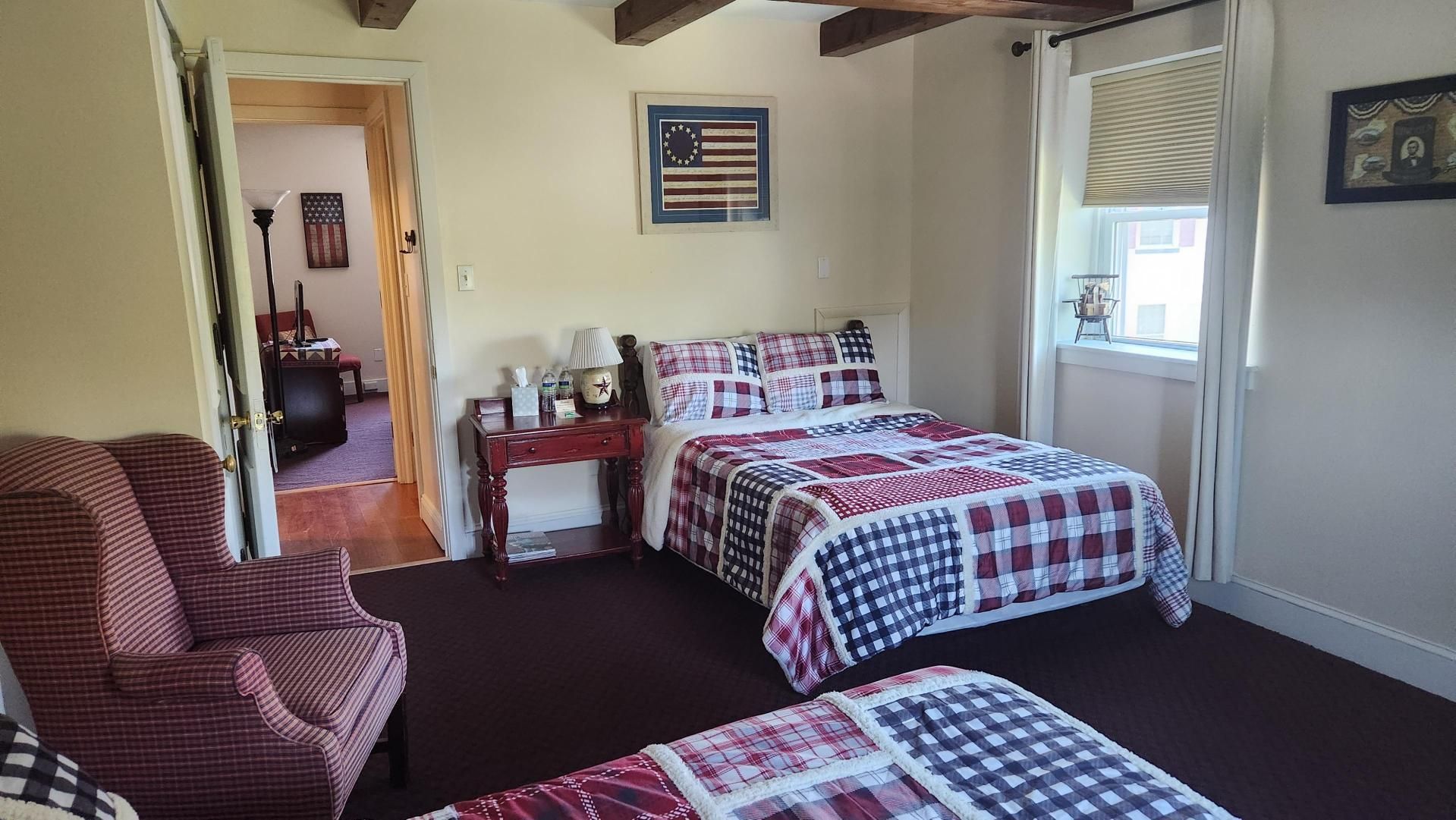 A bedroom with two beds , a chair , and a picture of an american flag on the wall.