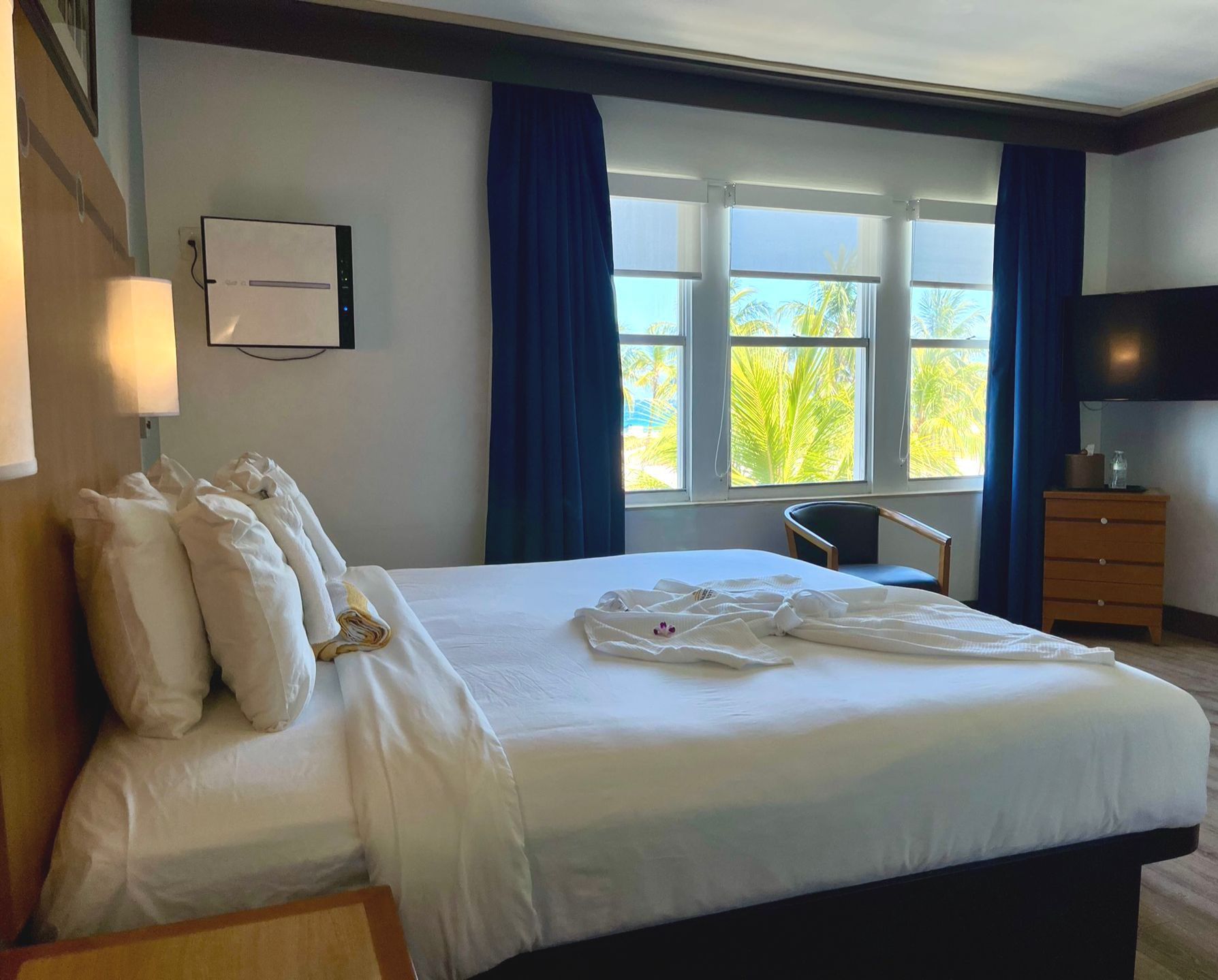 A hotel room with a king size bed , chair , dresser and television.