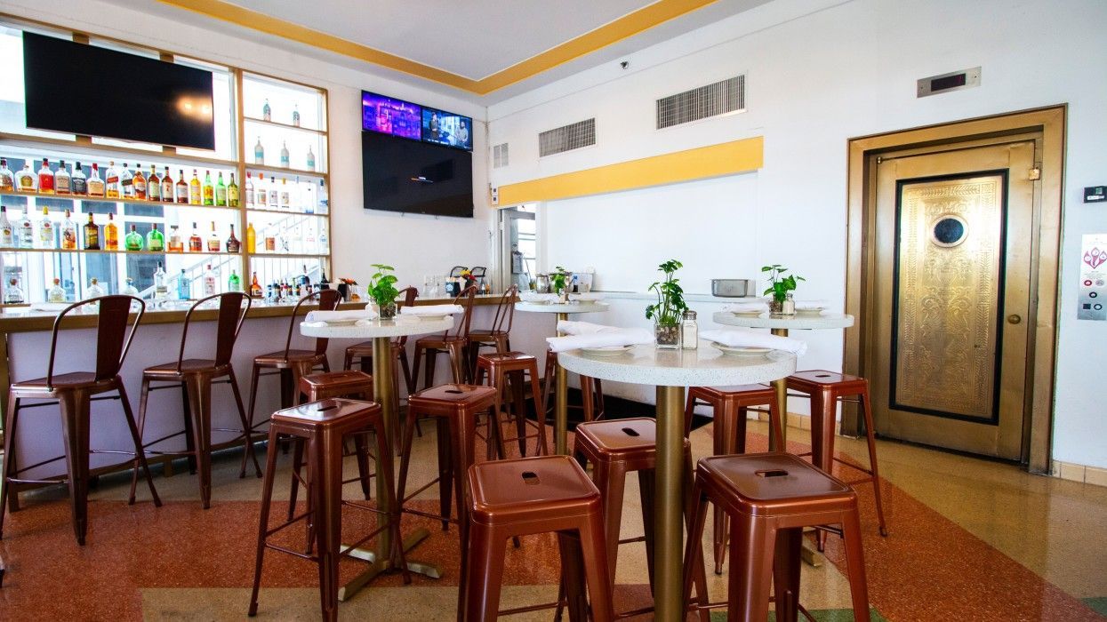 A restaurant with tables and stools and a bar.