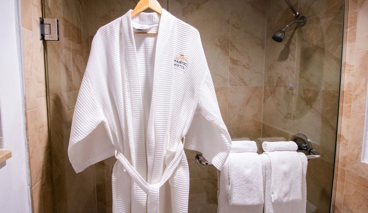 A white robe is hanging in a bathroom next to towels.
