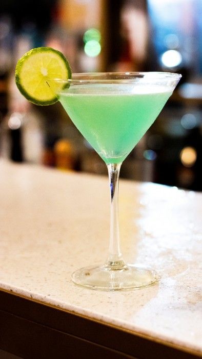 A green martini with a lime slice on a bar.