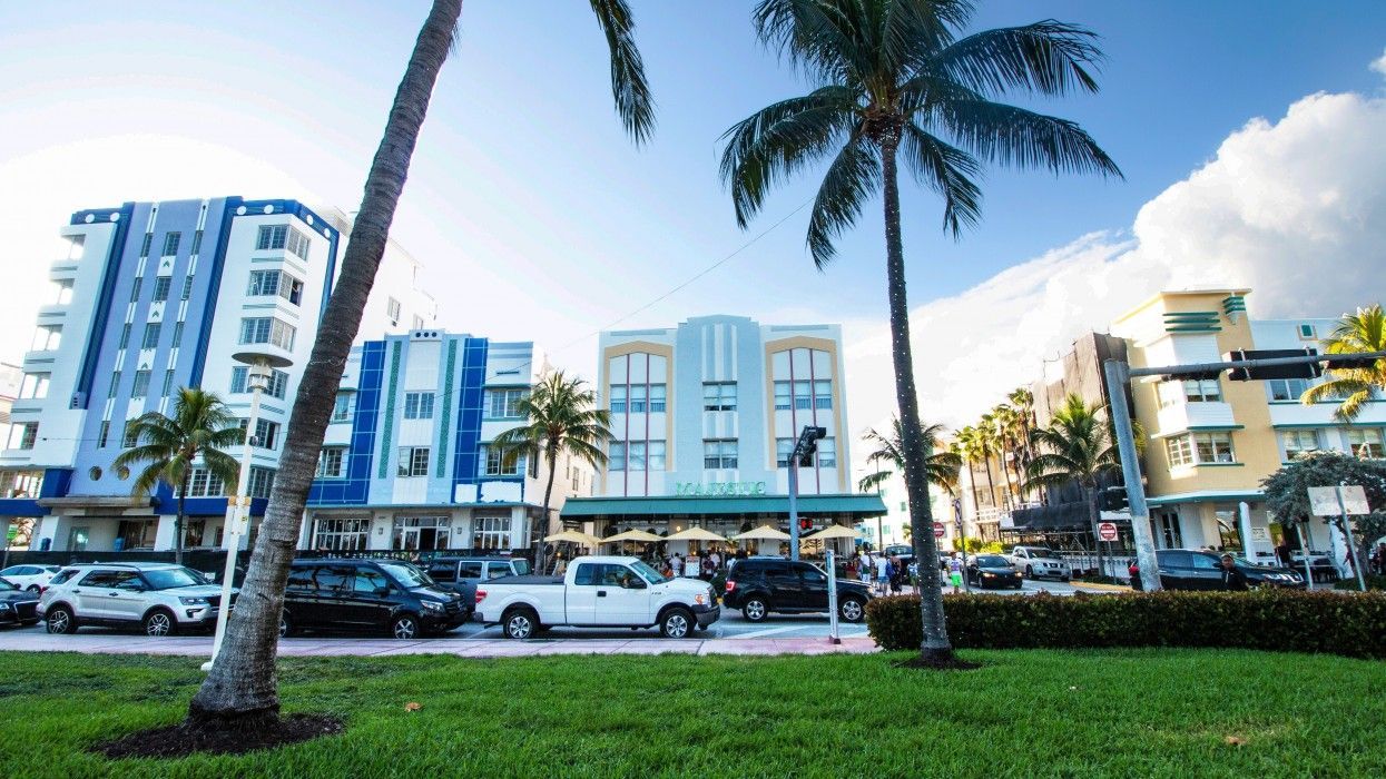 A city street with a lot of cars parked in front of a building and palm trees.