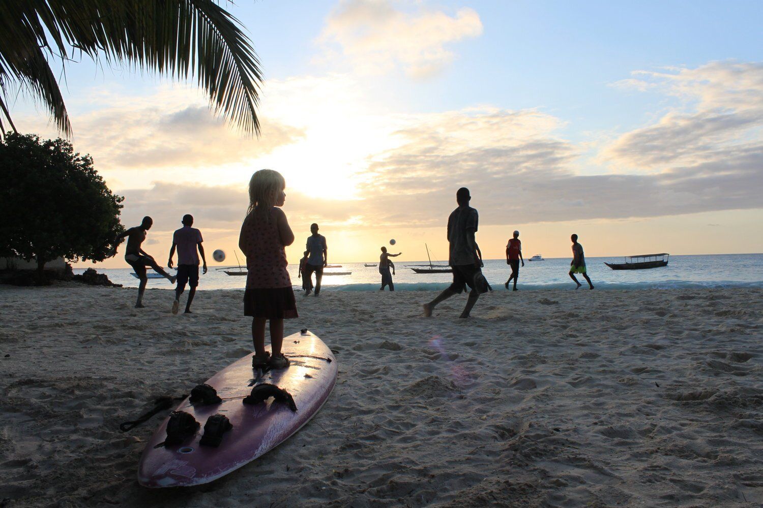 en gruppe mennesker spiller fodbold på en strand ved solnedgang.
