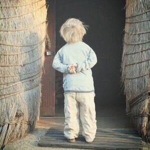 en lille dreng står i døren til en hytte.