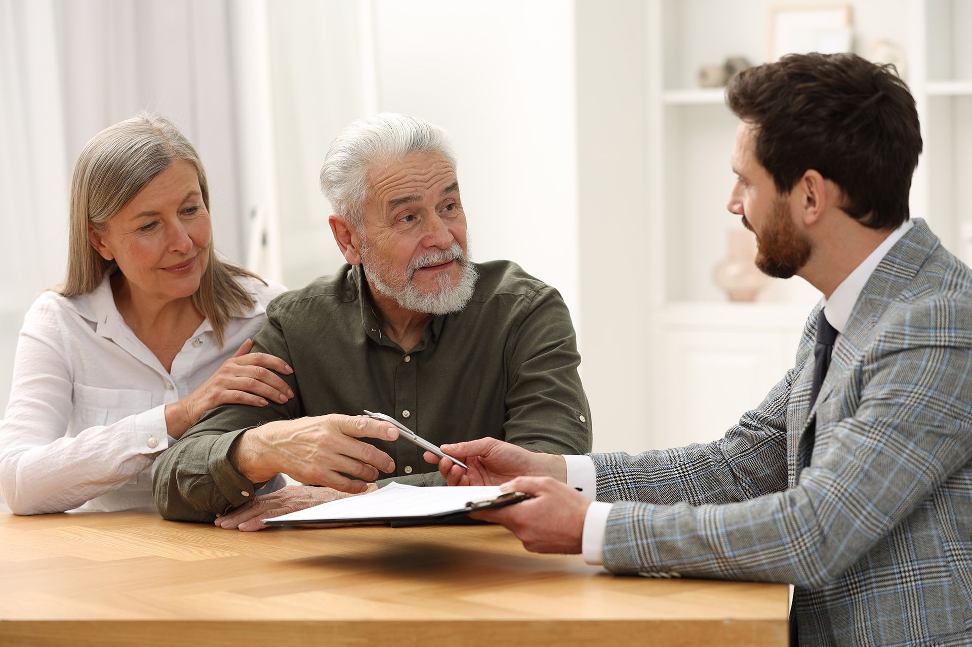 An elderly couple is sitting at a table talking to a man.