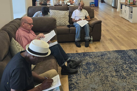 People seated on sofas in a lounge, reading papers and notebooks.