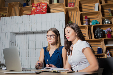 Two people working at a laptop in a modern office with shelves and books behind them