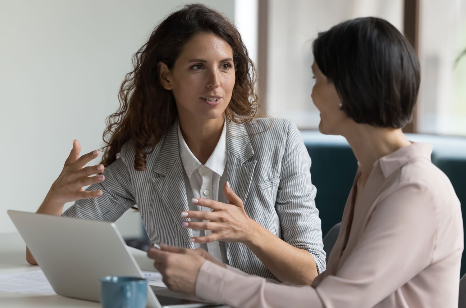 diverse female colleagues sit at desk discussing project details