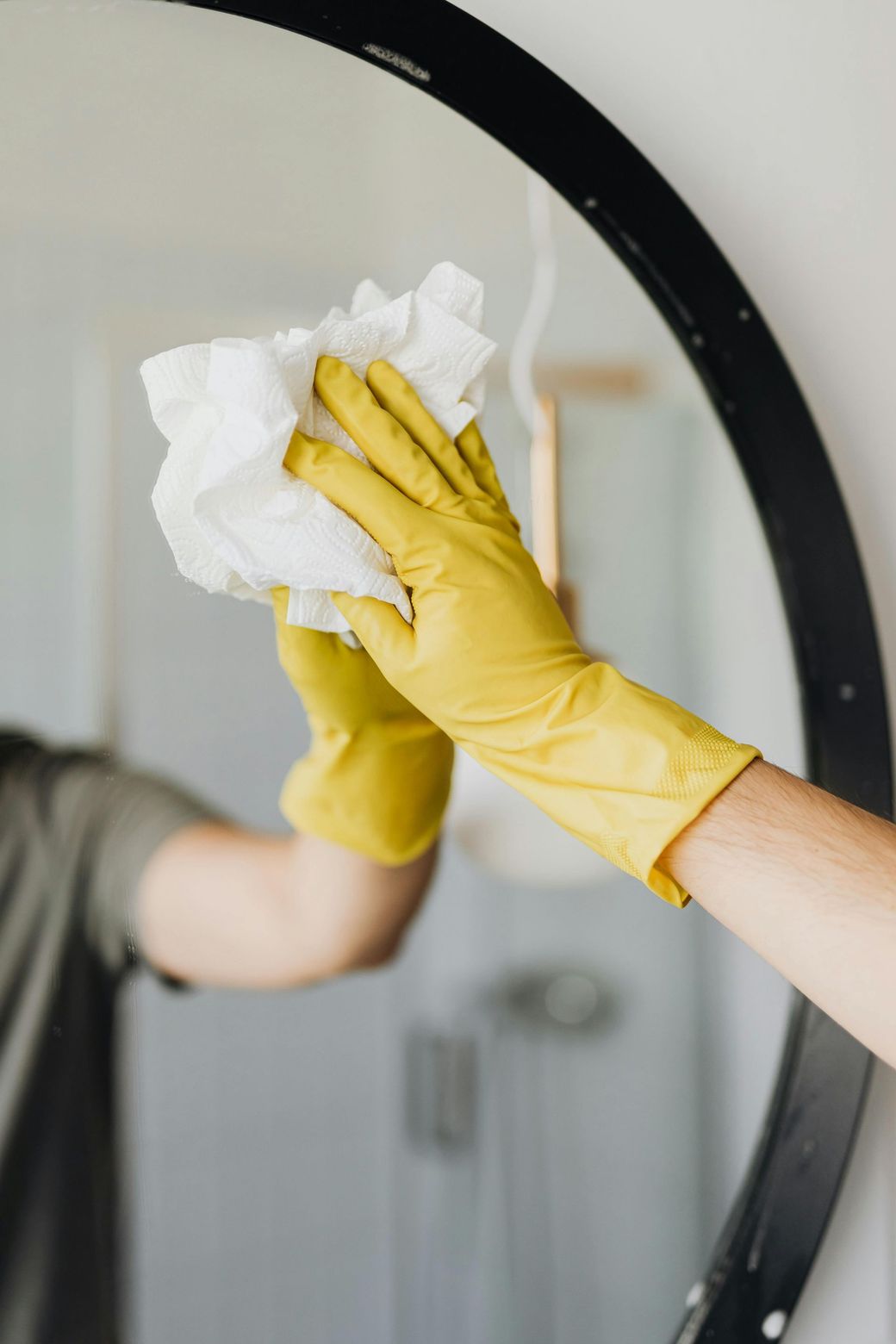 A person wearing yellow gloves is cleaning a mirror with a napkin.