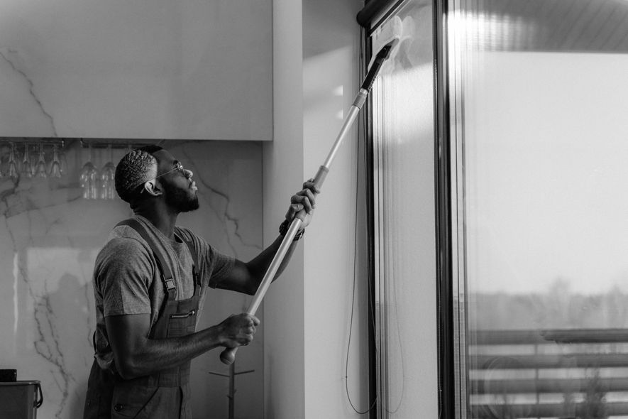 A man is cleaning a window with a mop in a black and white photo.