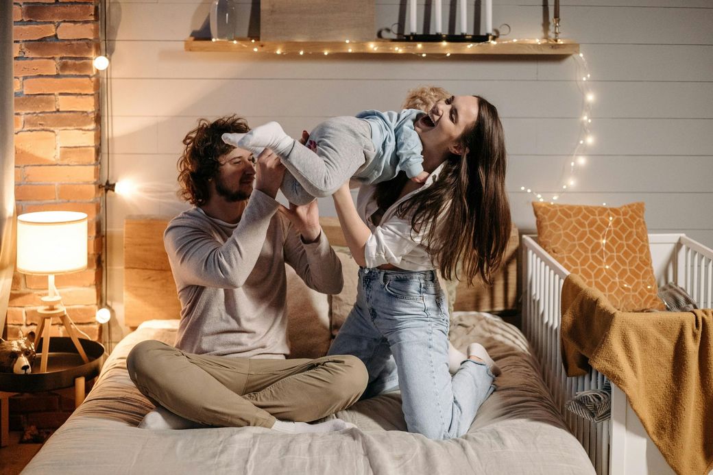 A man and a woman are sitting on a bed holding a baby.