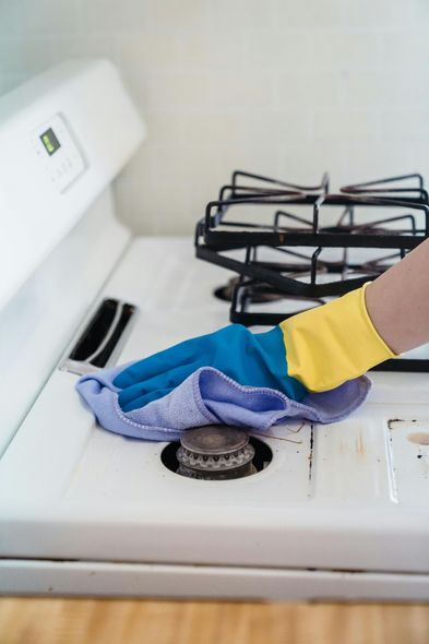 A person is cleaning a stove with a cloth and gloves.