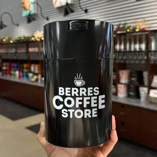 Black cylindrical coffee container held in hand with
