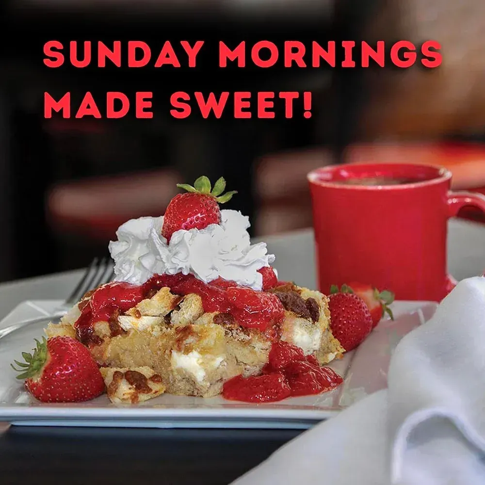 Fried breakfast pastry with strawberry sauce, whipped cream, and fresh strawberries. A red mug.