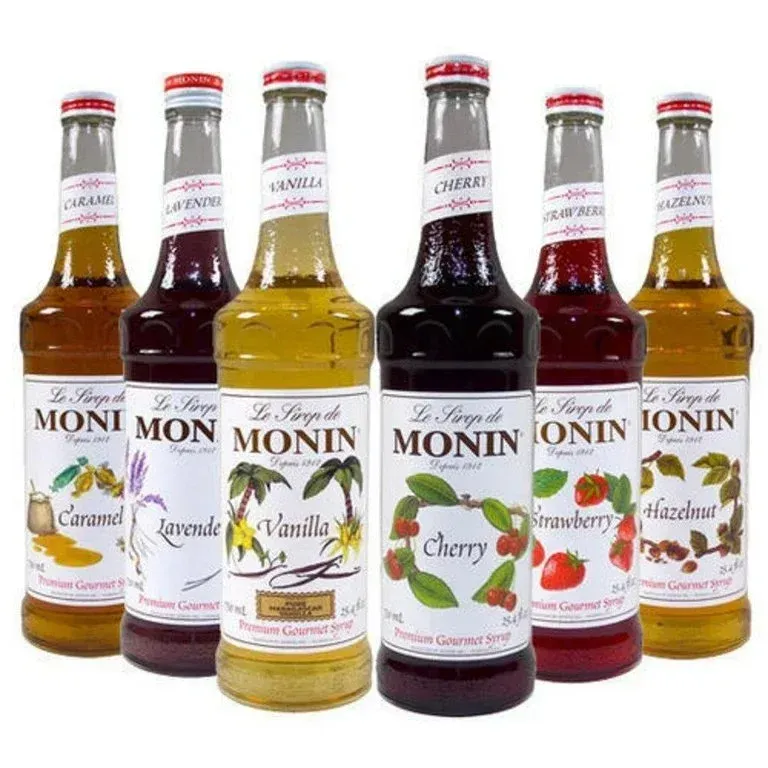 Six Monin syrup bottles, labeled caramel, lavender, vanilla, cherry, strawberry, and hazelnut, arranged in a row.