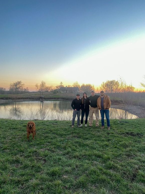 the owners of Long Creek RV Park posing for a picture in front of the pond with their golden retriever 